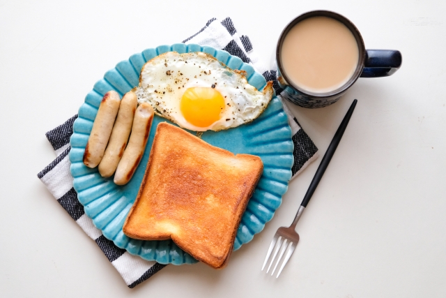 プレートに乗ったトースト、ソーセージ、目玉焼きとカフェオレの画像