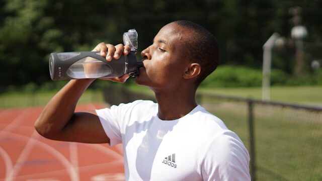 外国人男性が運動場でスポーツドリンクを飲んでいる画像