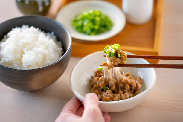 ご飯と納豆が食卓に並んでいて、箸で納豆を持ち上げている画像