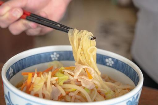 野菜の乗った味噌ラーメンの麺を箸で持ち上げている画像