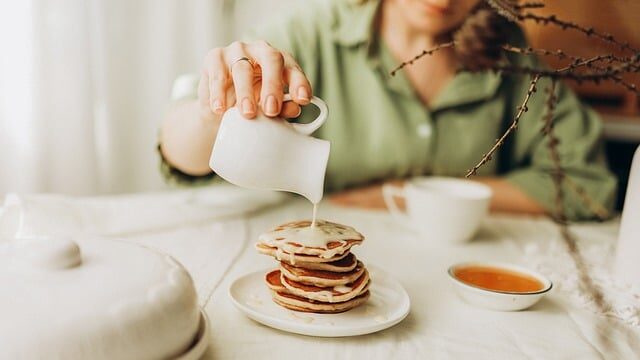 重なった小さいパンケーキに、女性が片手で練乳をかけている画像