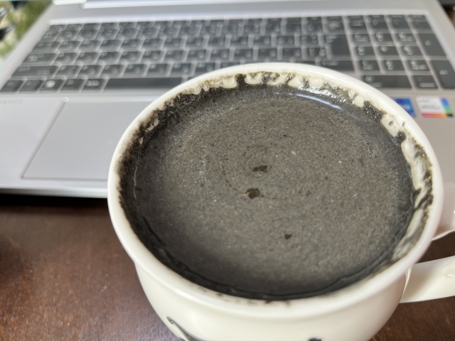 ノートパソコンの前に置かれたマグカップに入ったチャコールコーヒーの画像