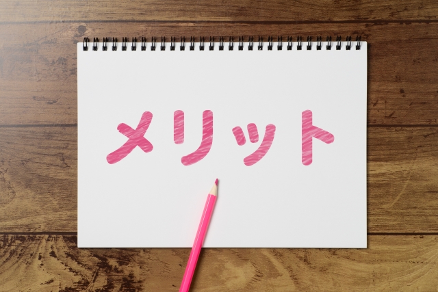 白いノートにピンク色で書かれたメリットの文字とピンクの色鉛筆の画像