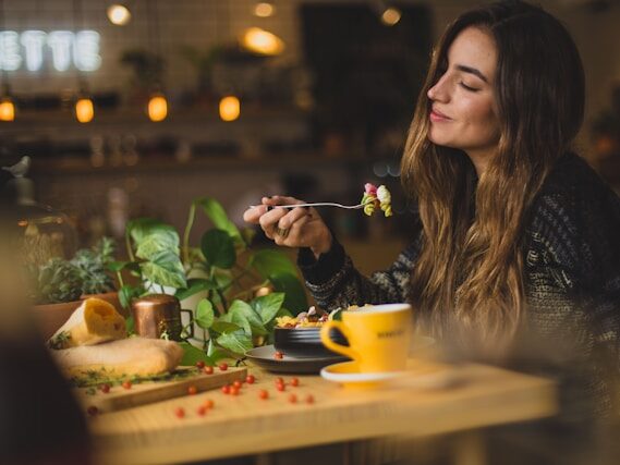 ロングヘアーの外国人女性が、食べ物が刺さっているフォークをもって微笑んでいる画像