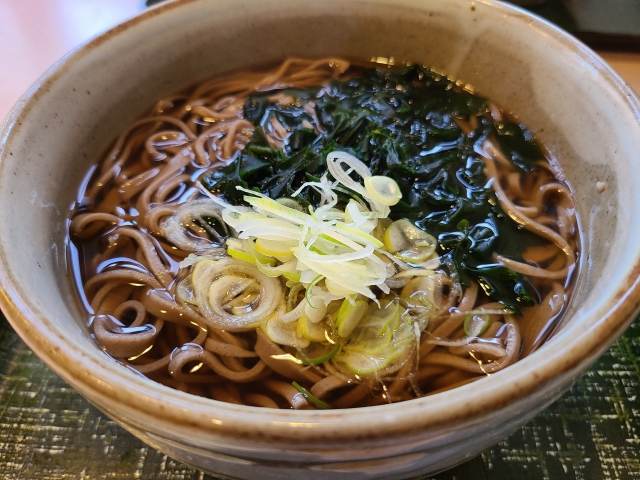 丼ぶりに九条ネギとわかめがトッピングされた温かいそばの画像。