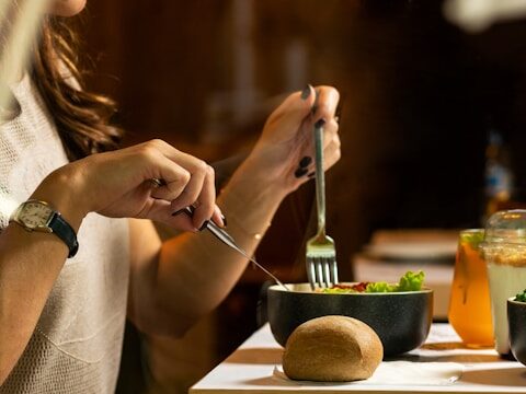 女性が銀のスプーンとフォークで食事している画像