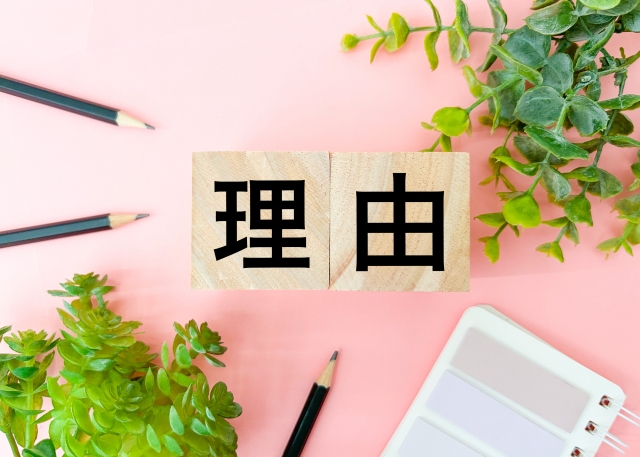 「理由」と書かれたブロックと鉛筆と人工植物の画像。